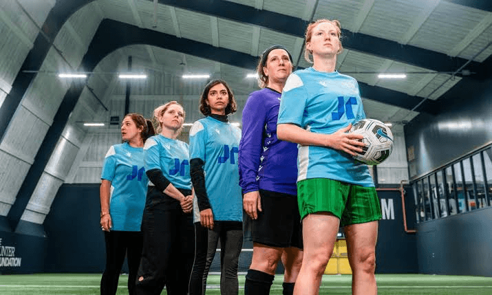 Athletes standing together indoors, one holding a soccer ball